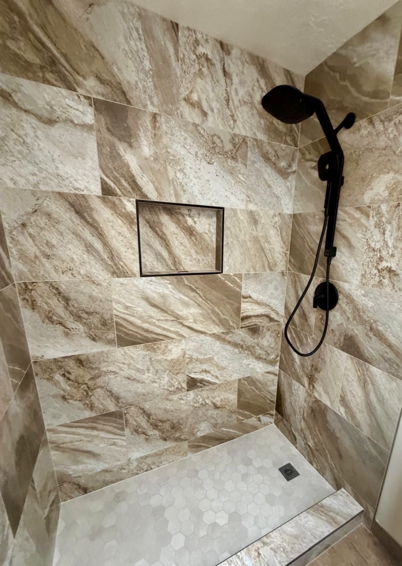 Warm stone tile shower with hexagonal floor and black fixtures